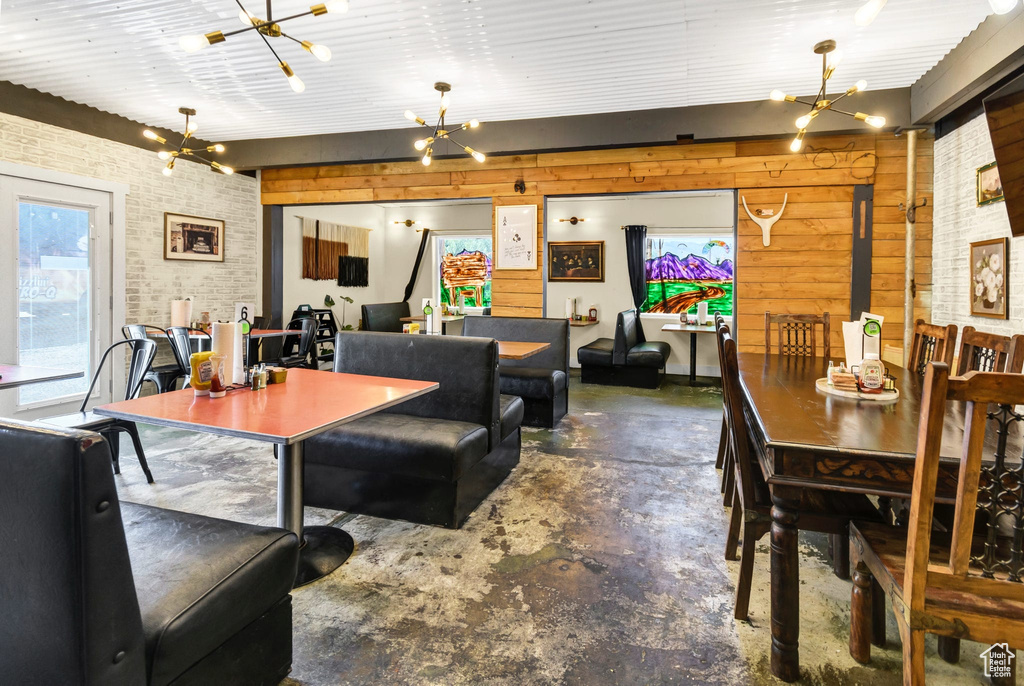 Dining room with a chandelier, concrete floors, brick wall, and wood walls