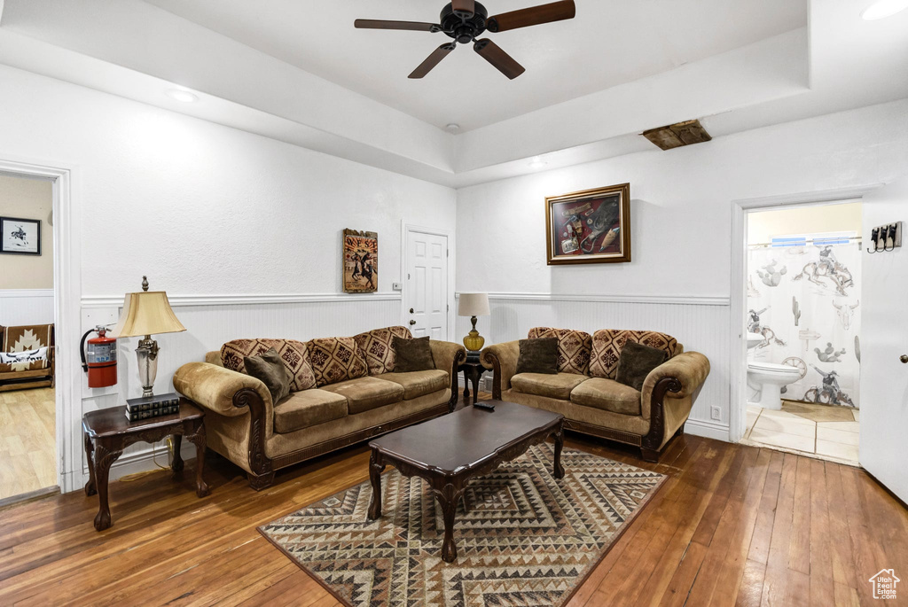 Living room featuring ceiling fan, hardwood / wood-style flooring, wainscoting, and a tray ceiling