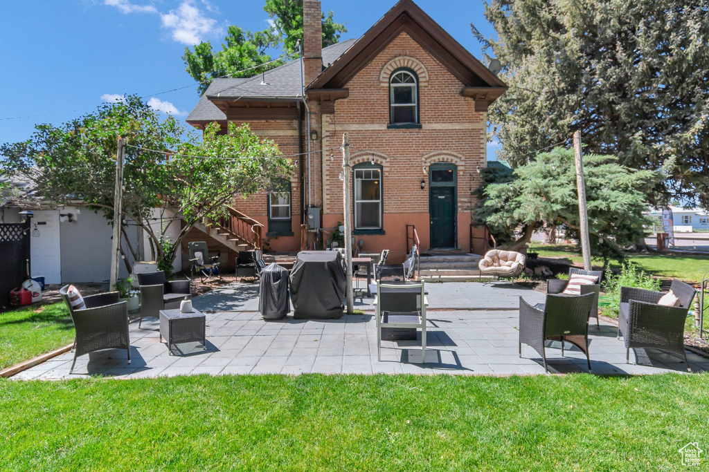 Rear view of property with brick siding, a yard, a chimney, a patio, and stairway