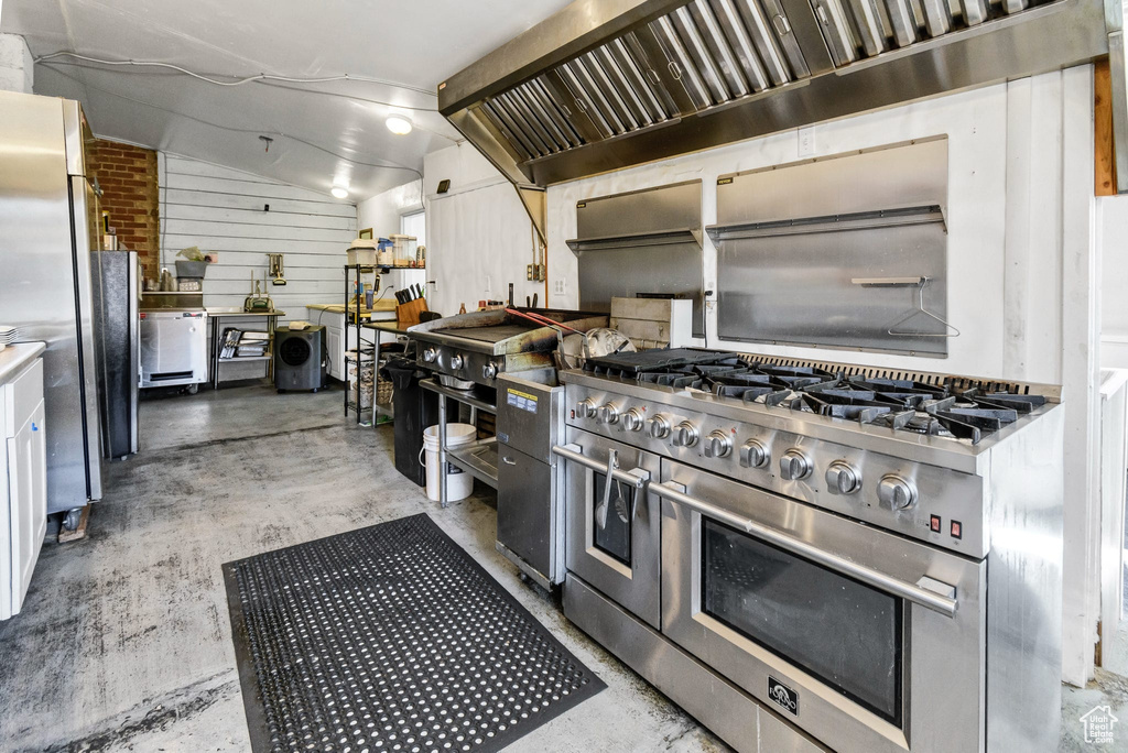 Kitchen with stainless steel appliances, wall chimney exhaust hood, concrete flooring, and vaulted ceiling