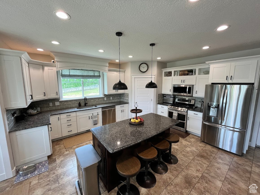 Kitchen with appliances with stainless steel finishes, tasteful backsplash, white cabinets, a kitchen bar, and a textured ceiling