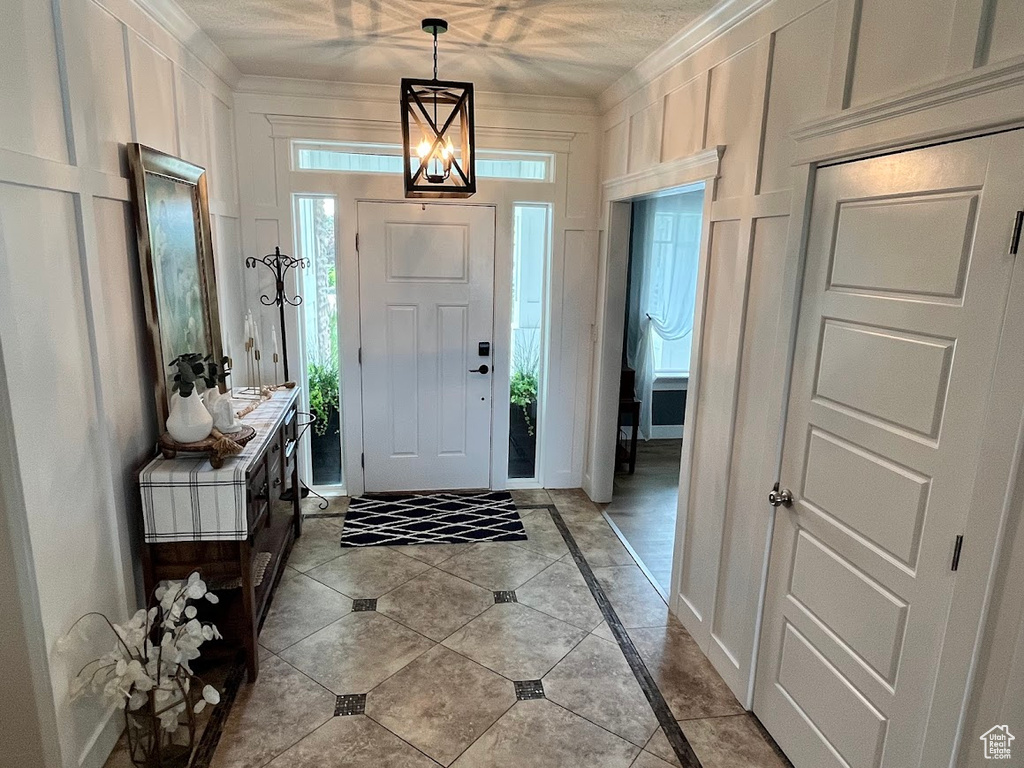 Foyer with inlaid floor details, a decorative wall, light tile patterned floors, and crown molding