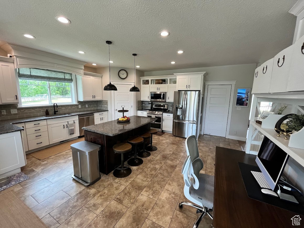 Kitchen with appliances with stainless steel finishes, tasteful backsplash, a center island, a breakfast bar area, and a textured ceiling