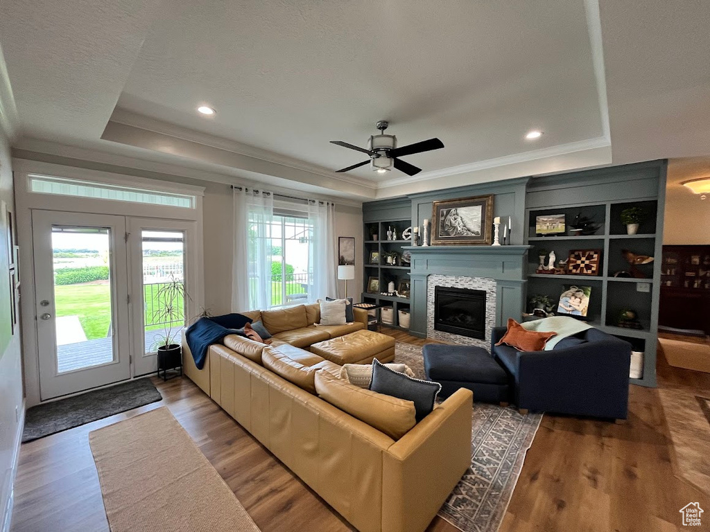 Living area with a tray ceiling, crown molding, wood finished floors, a glass covered fireplace, and ceiling fan