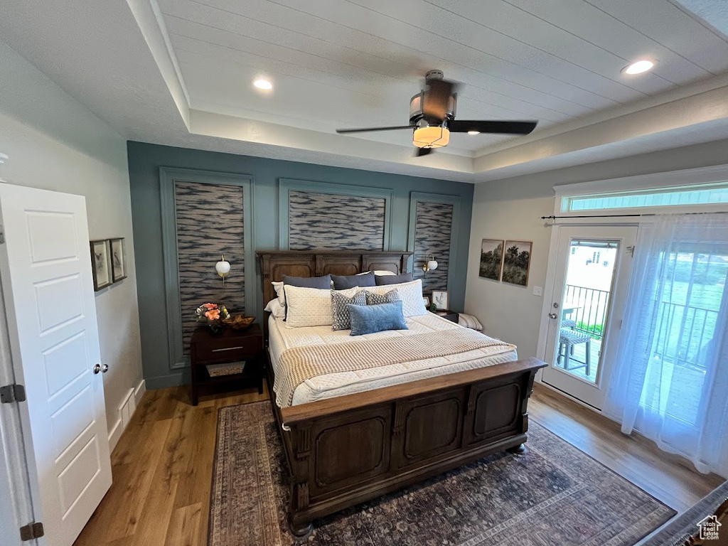 Bedroom with a tray ceiling, access to outside, light wood-style floors, and a ceiling fan