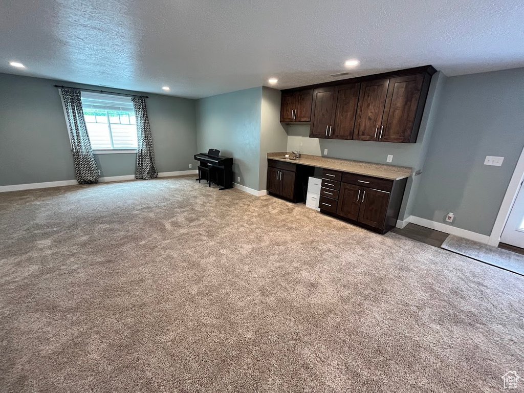 Kitchen featuring a textured ceiling, dark brown cabinets, light countertops, light colored carpet, and recessed lighting