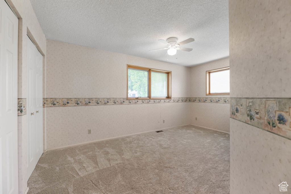 Empty room with a ceiling fan, a textured ceiling, carpet flooring, and wallpapered walls