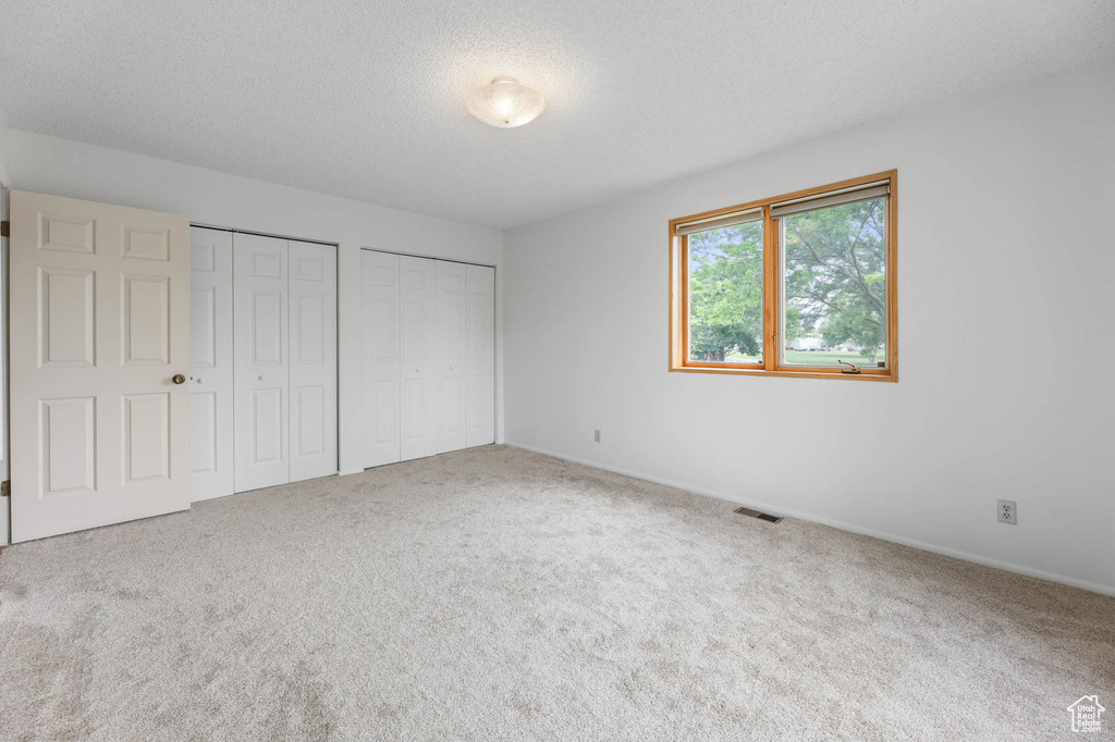 Unfurnished bedroom featuring two closets, carpet floors, and a textured ceiling