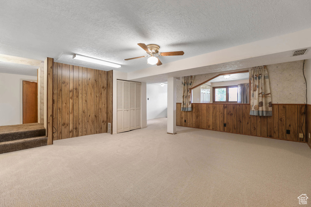 Basement featuring wood walls, carpet flooring, a textured ceiling, stairs, and ceiling fan