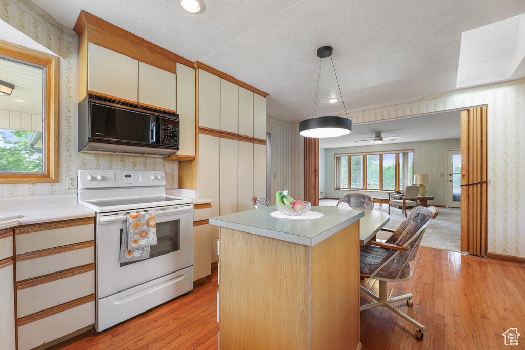 Kitchen with black microwave, white electric range, wallpapered walls, light countertops, and light wood-style floors