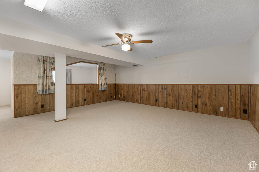Spare room with wainscoting, wood walls, carpet, a ceiling fan, and a textured ceiling