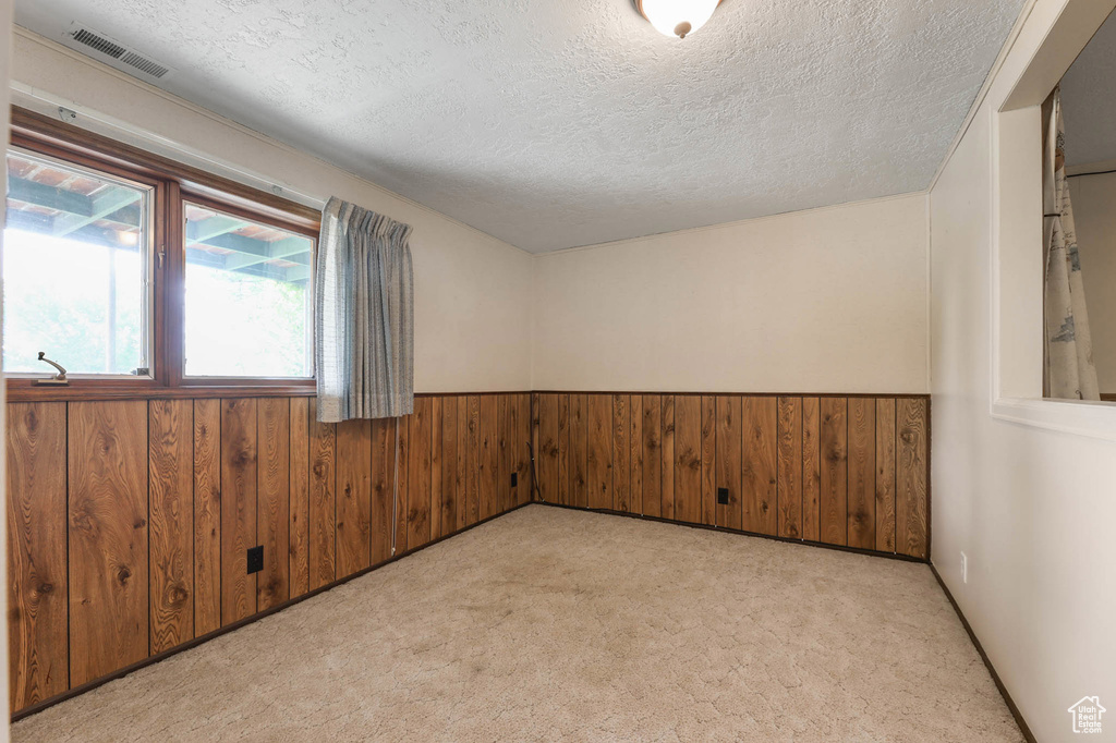 Carpeted spare room featuring wood walls, a textured ceiling, and wainscoting