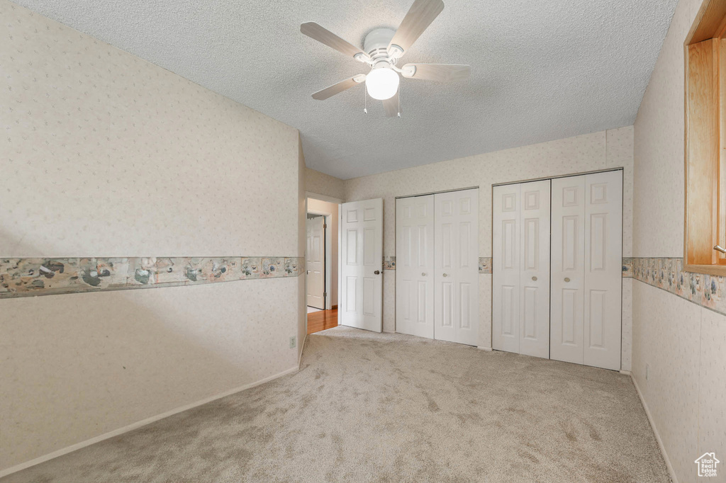 Unfurnished bedroom with two closets, carpet floors, wallpapered walls, a textured ceiling, and a ceiling fan