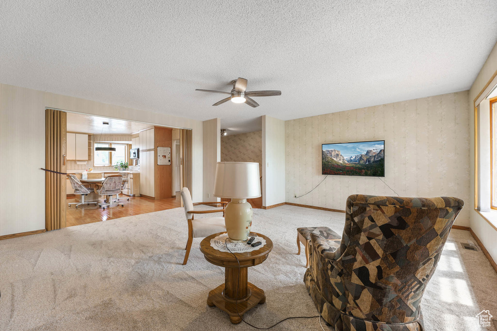 Sitting room with carpet, a ceiling fan, a textured ceiling, and wallpapered walls