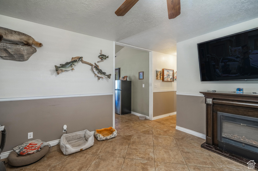 Living room with ceiling fan, a textured ceiling, light tile patterned floors, and a glass covered fireplace
