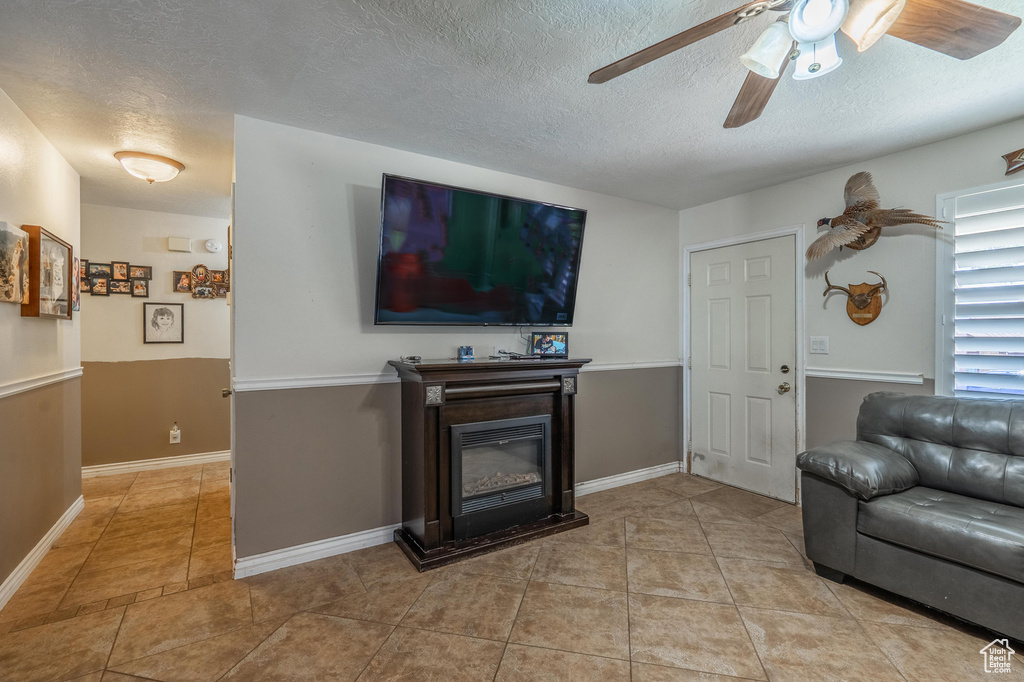 Living room with ceiling fan, a textured ceiling, a glass covered fireplace, and light tile patterned flooring