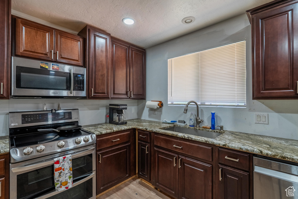 Kitchen with appliances with stainless steel finishes, light stone countertops, light wood-style floors, a textured ceiling, and recessed lighting