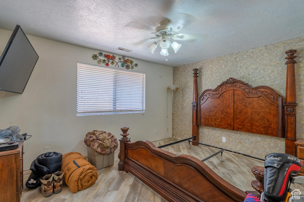 Bedroom with wood finished floors, a textured ceiling, ceiling fan, and wallpapered walls