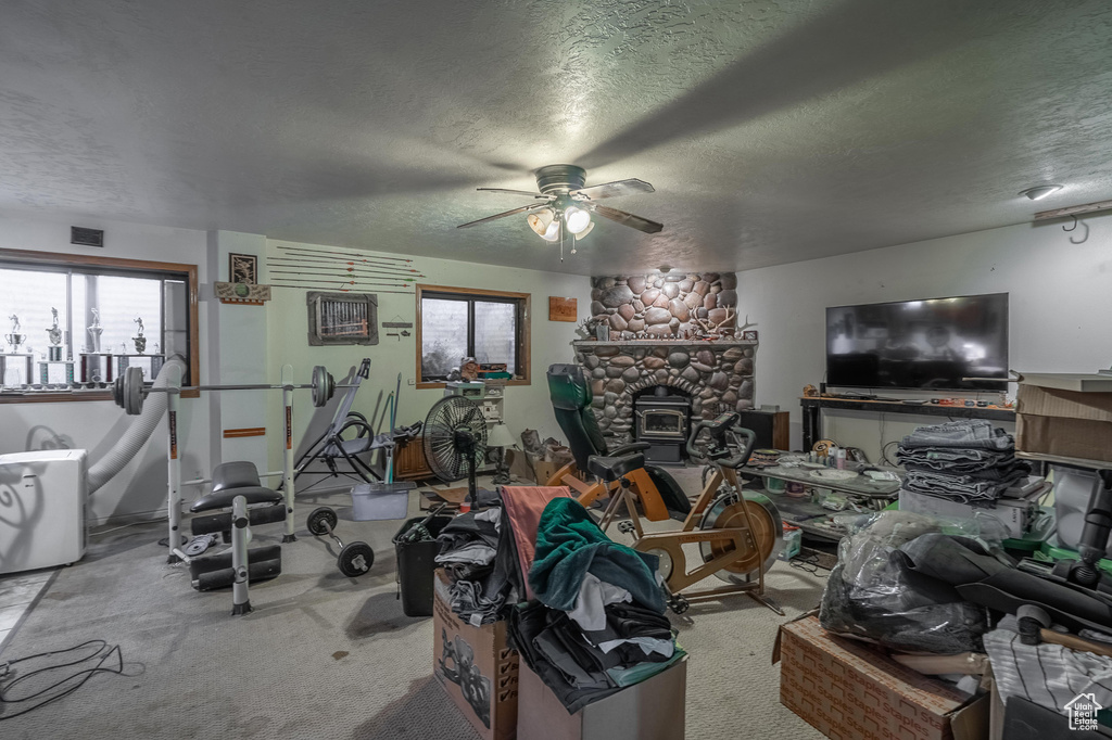 Exercise area featuring a textured ceiling, a ceiling fan, carpet flooring, and a glass covered fireplace