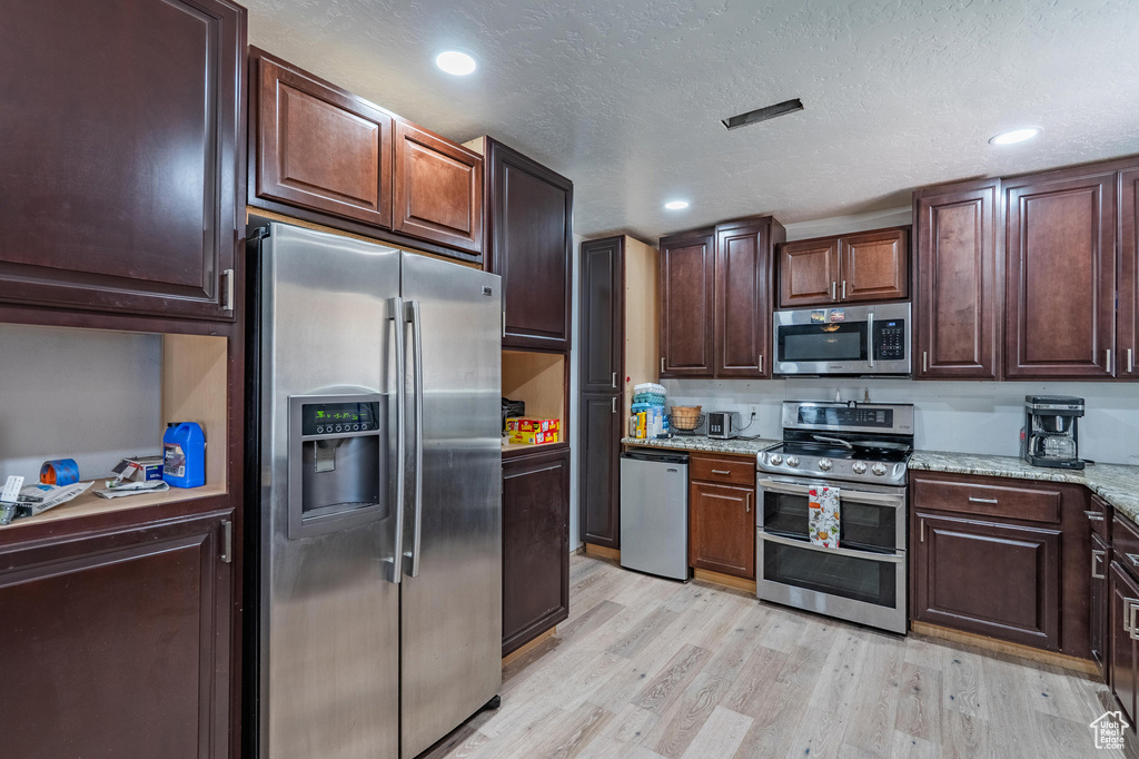 Kitchen featuring appliances with stainless steel finishes, light wood finished floors, light stone counters, dark brown cabinetry, and recessed lighting