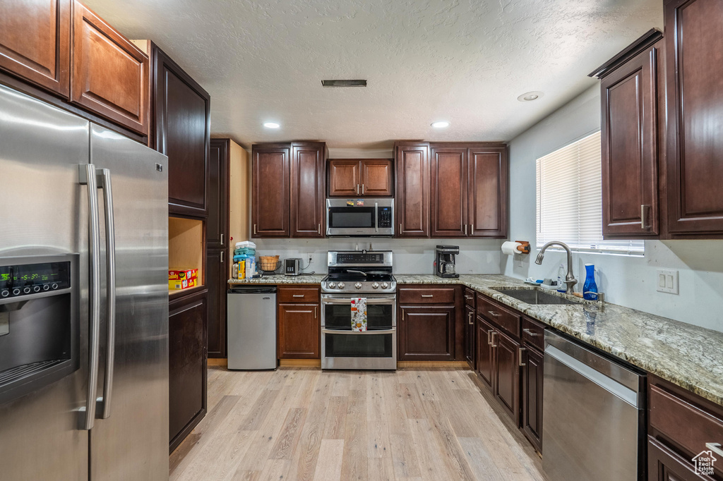 Kitchen featuring appliances with stainless steel finishes, light wood-style floors, light stone countertops, and dark brown cabinetry