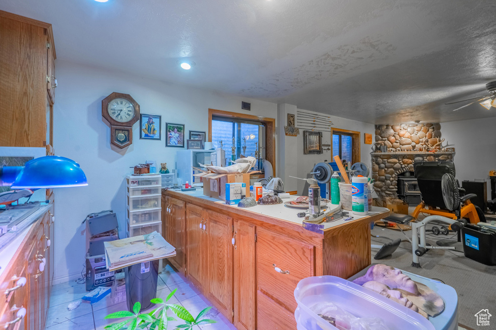 Kitchen featuring open floor plan, a wood stove, brown cabinets, light countertops, and a ceiling fan