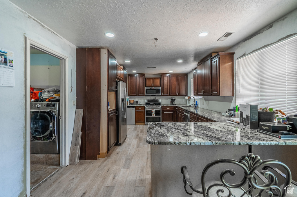 Kitchen with appliances with stainless steel finishes, washer / dryer, light wood finished floors, a peninsula, and a textured ceiling