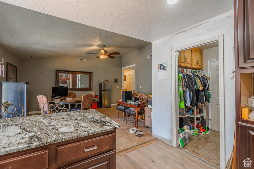 Kitchen featuring freestanding refrigerator, a ceiling fan, a textured ceiling, vaulted ceiling, and light wood finished floors