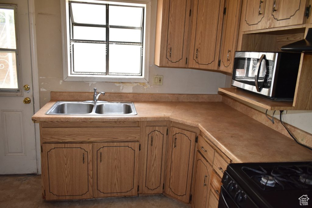 Kitchen featuring stainless steel microwave, light countertops, exhaust hood, and brown cabinets