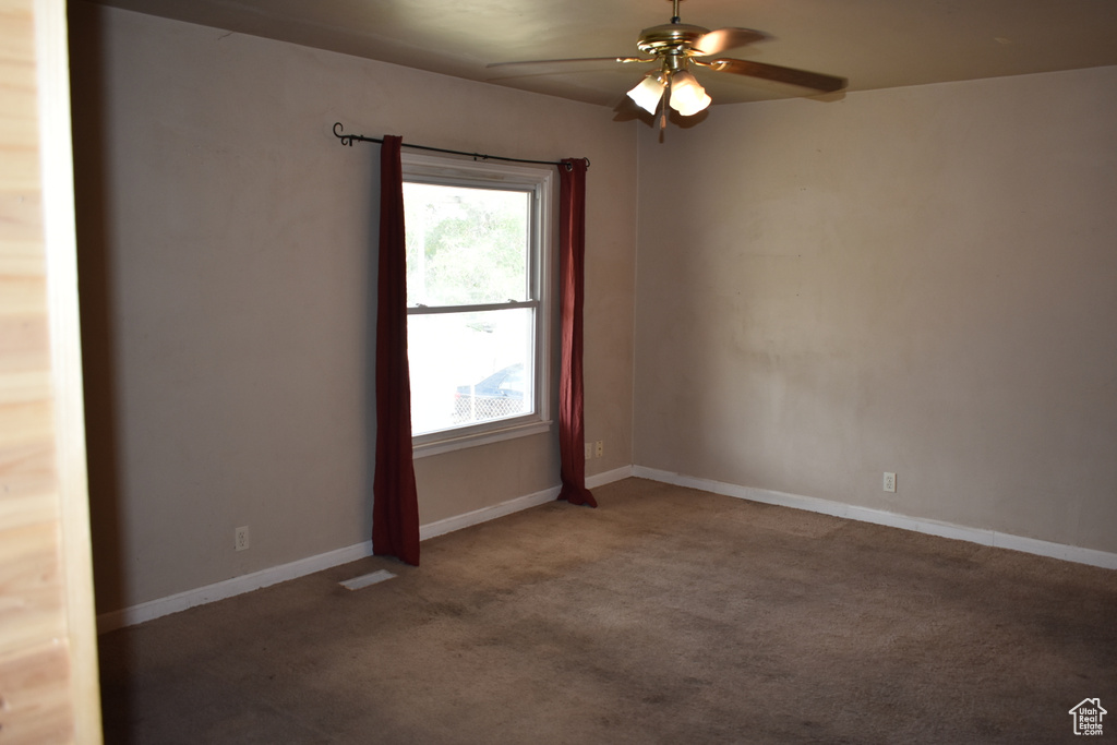 Carpeted empty room featuring ceiling fan and baseboards