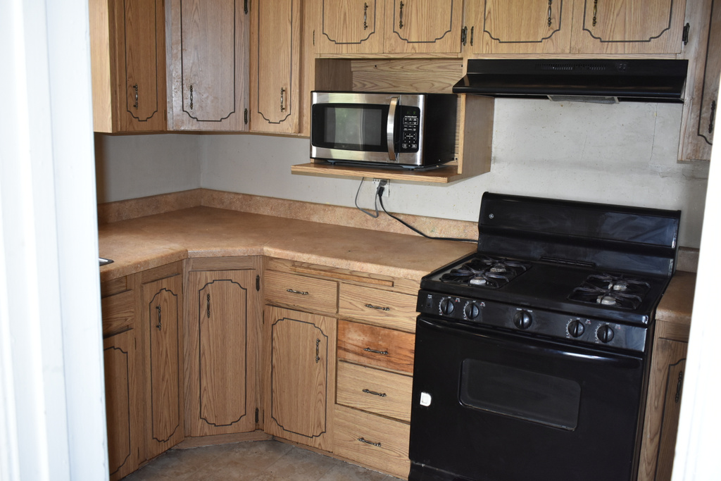 Kitchen featuring black gas stove, stainless steel microwave, under cabinet range hood, light countertops, and brown cabinets