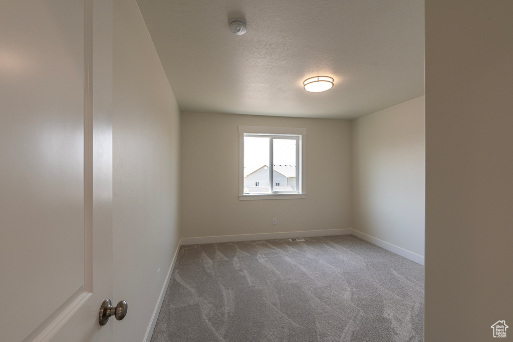 Spare room featuring carpet floors, a smoke detector, and a textured ceiling