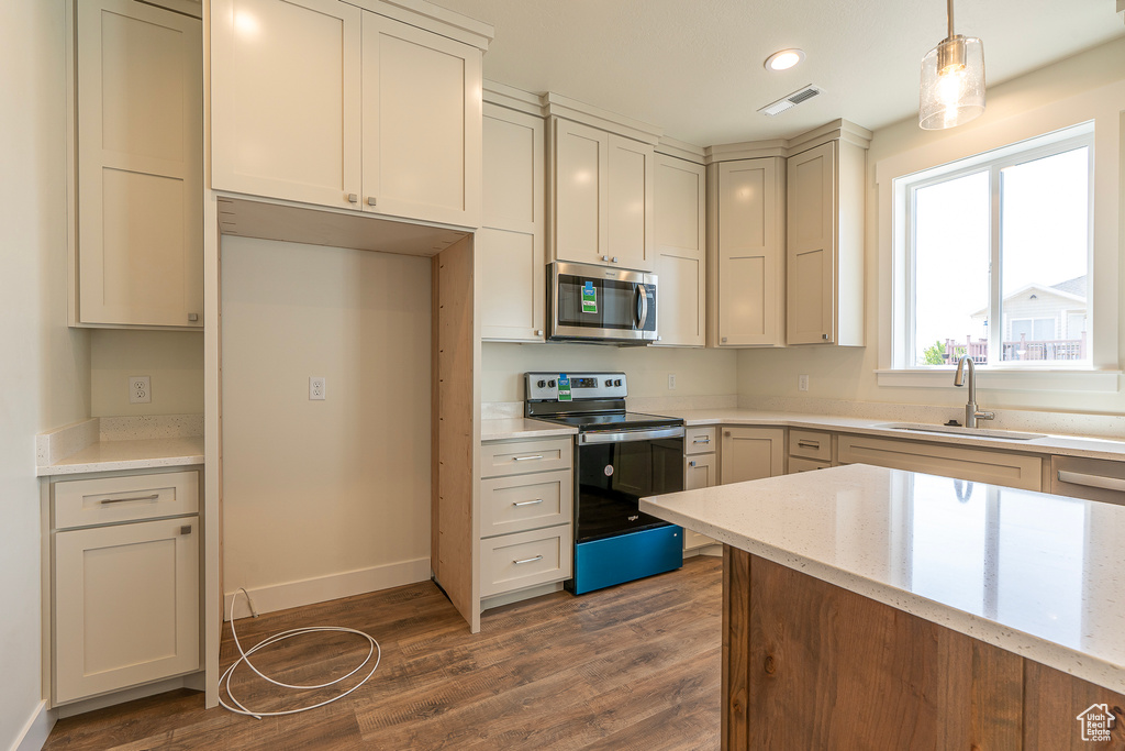 Kitchen with appliances with stainless steel finishes, dark wood-type flooring, light stone countertops, decorative light fixtures, and recessed lighting