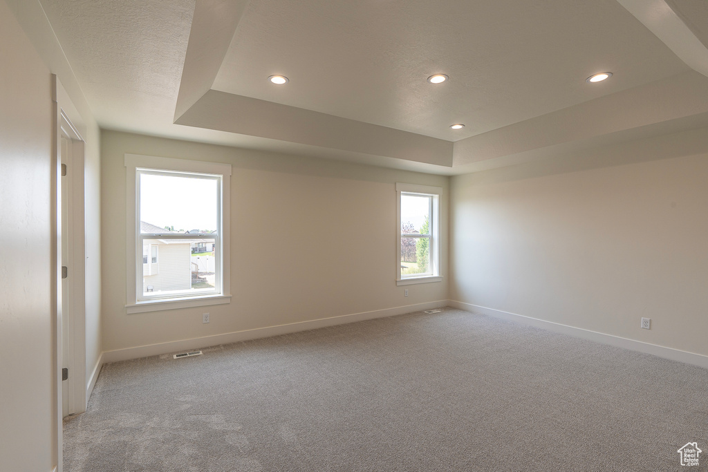 Empty room featuring recessed lighting, a raised ceiling, and light carpet