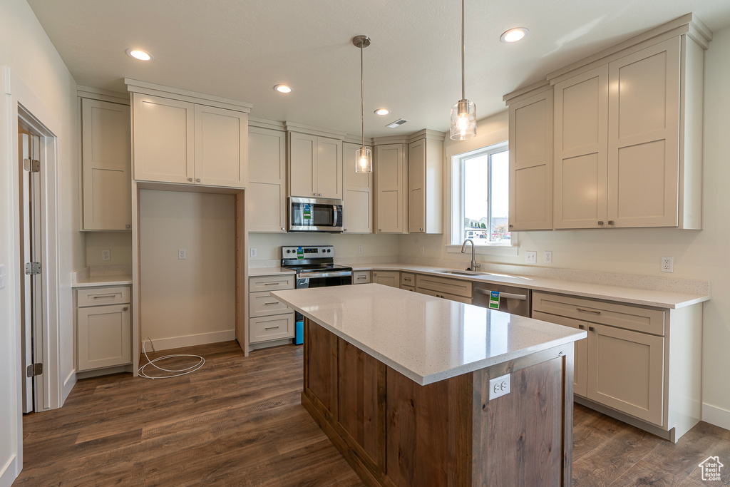 Kitchen with appliances with stainless steel finishes, dark wood-style flooring, light countertops, a center island, and recessed lighting