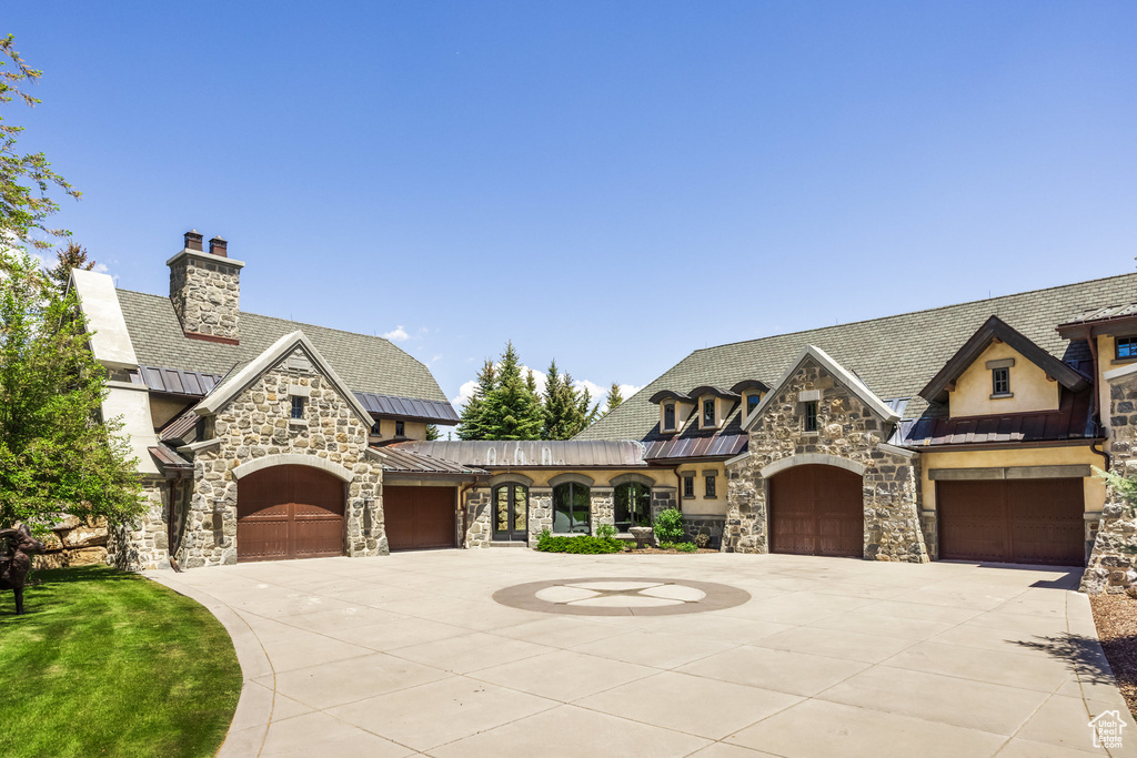 View of front of house with a standing seam roof, stone siding, driveway, and a metal roof