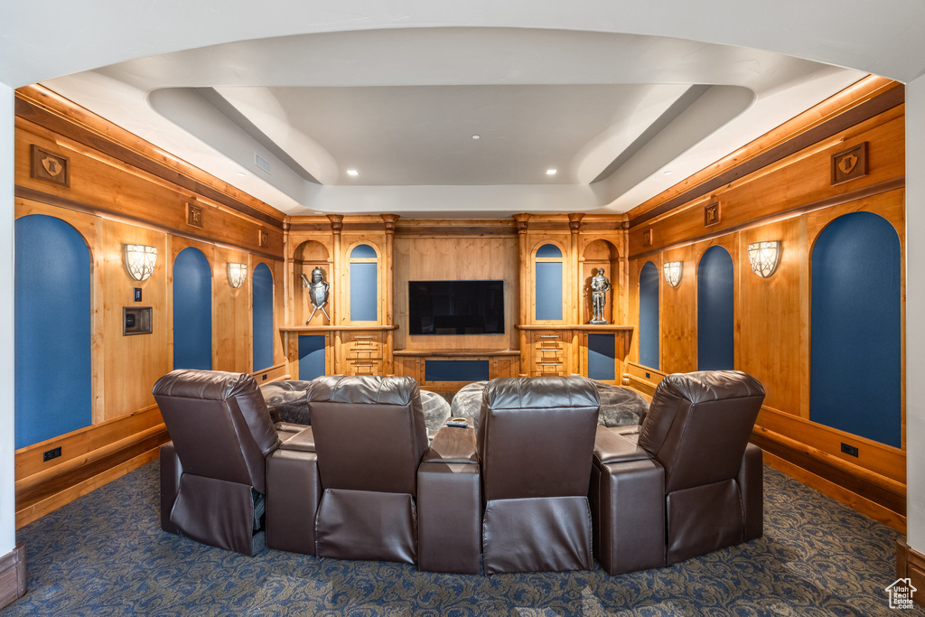 Home theater featuring a raised ceiling, wooden walls, carpet, and arched walkways