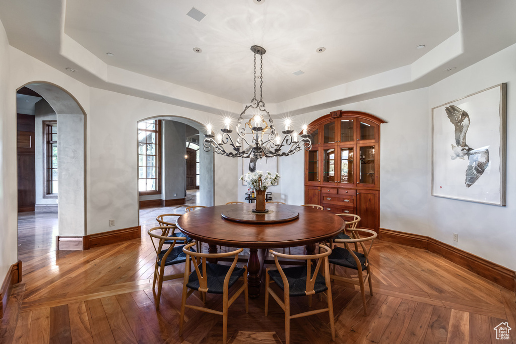 Dining area featuring arched walkways, a raised ceiling, a chandelier, and hardwood / wood-style flooring