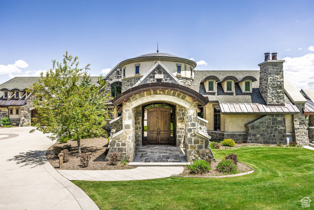 View of front of house featuring stone siding, stucco siding, a front yard, a chimney, and driveway