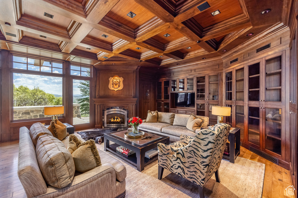 Living area with a wooden ceiling with exposed beams, wooden walls, ornamental molding, a lit fireplace, and light wood-style floors