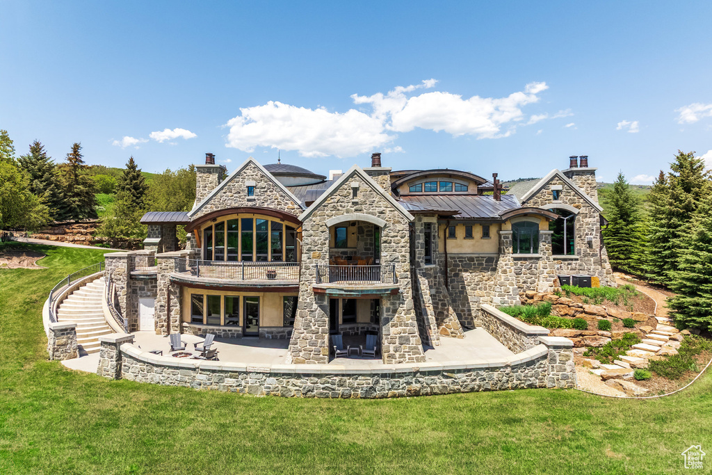 Rear view of property with a balcony, stone siding, and a yard