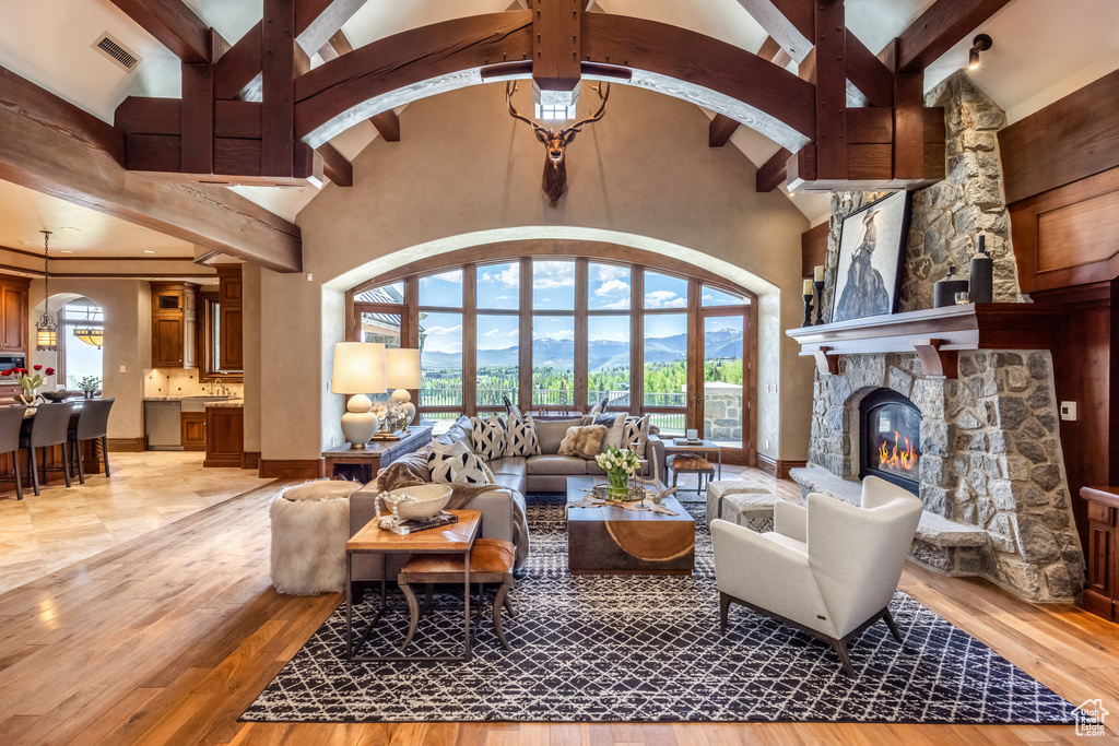 Living room featuring high vaulted ceiling, plenty of natural light, a fireplace, beam ceiling, and light wood finished floors