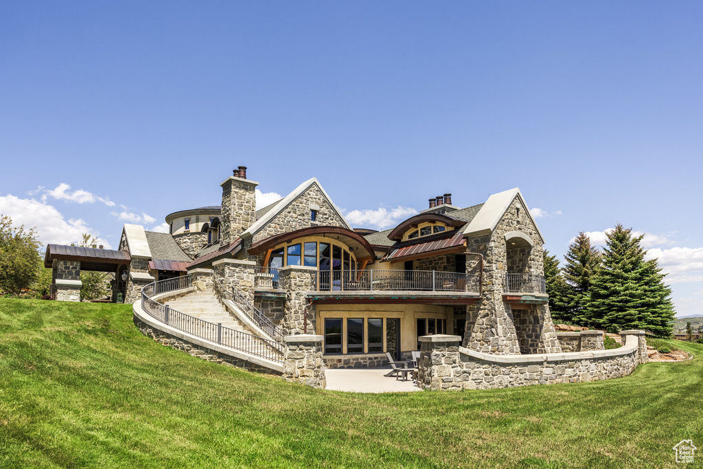 Back of house featuring stone siding, a balcony, a lawn, and a chimney