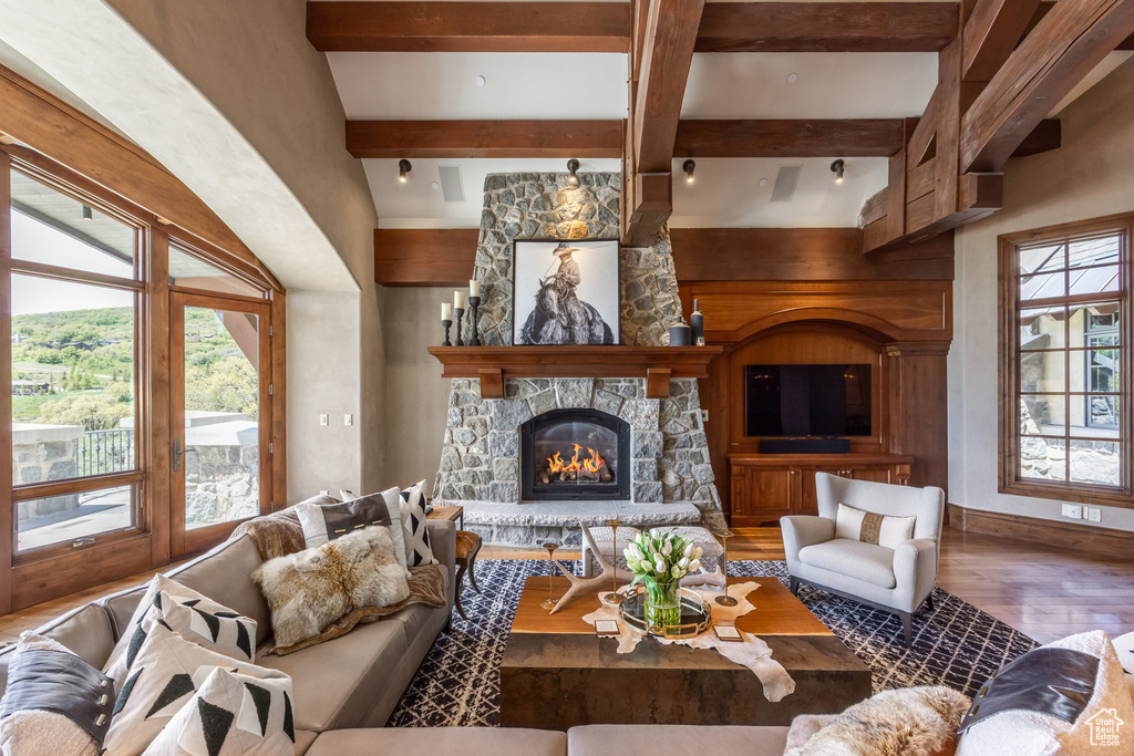 Living room featuring wood finished floors, a stone fireplace, and beam ceiling