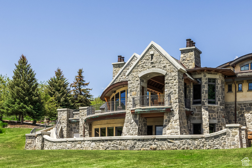 Rear view of property with a balcony, stone siding, a yard, and a chimney