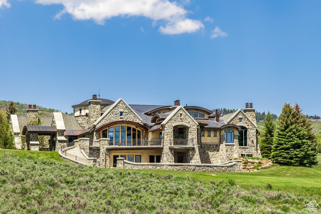 Back of property featuring a balcony, stone siding, a standing seam roof, a chimney, and a metal roof