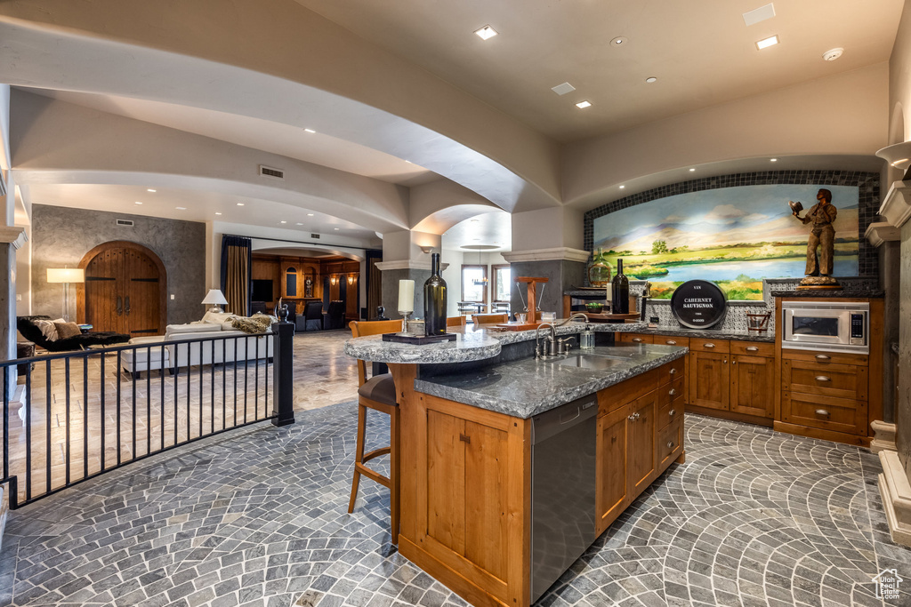 Kitchen featuring dishwashing machine, arched walkways, stainless steel microwave, a breakfast bar, and open floor plan