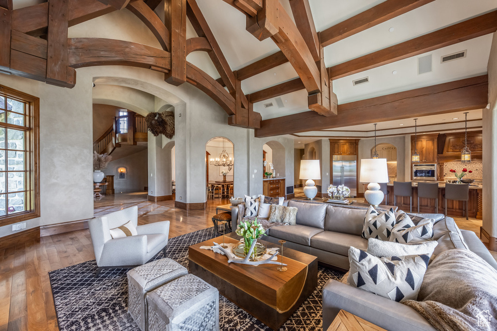 Living area with arched walkways, wood-type flooring, beam ceiling, high vaulted ceiling, and a chandelier