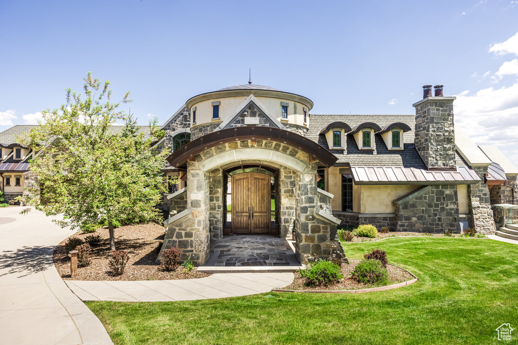 View of front facade with stone siding, stucco siding, a chimney, and a front yard