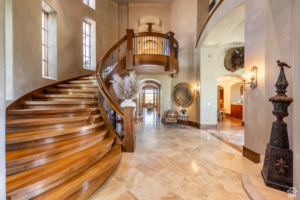 Foyer with arched walkways, a towering ceiling, marble tiled flooring, and stairs